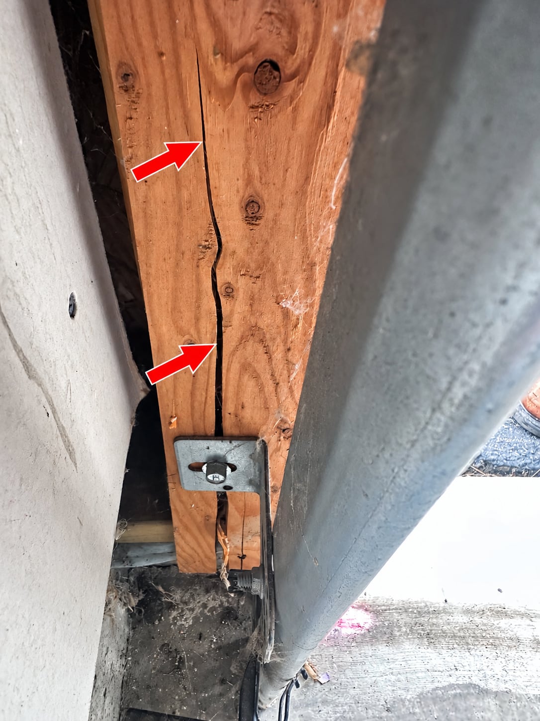 Cracked wood garage door jamb with a split running through a track bracket mount.