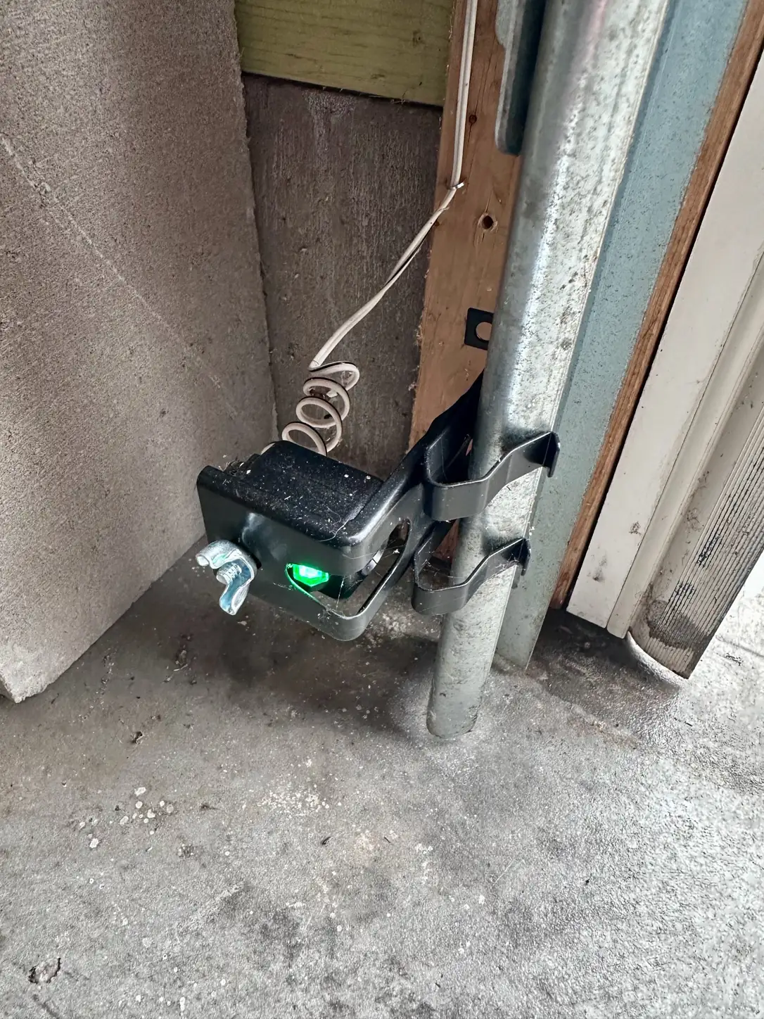 Garage door safety sensor with a green indicator light, mounted to the vertical track near the floor.