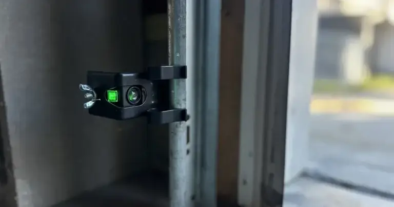 Garage door safety sensor with green indicator light, sunlight in the background