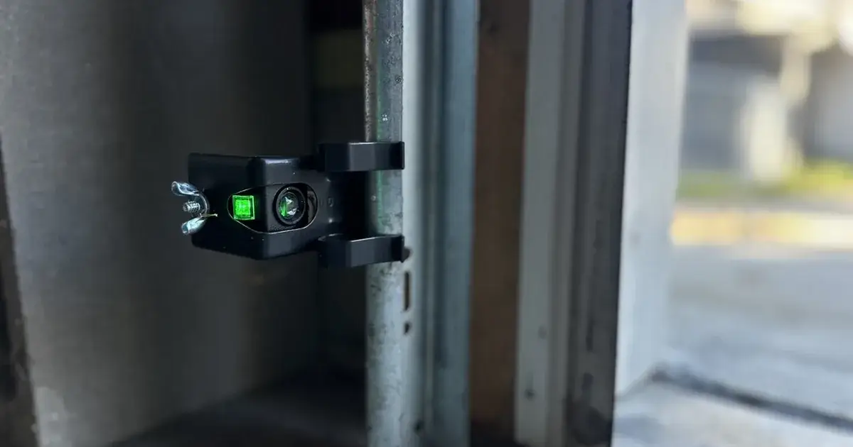 Garage door safety sensor with green indicator light, sunlight in the background