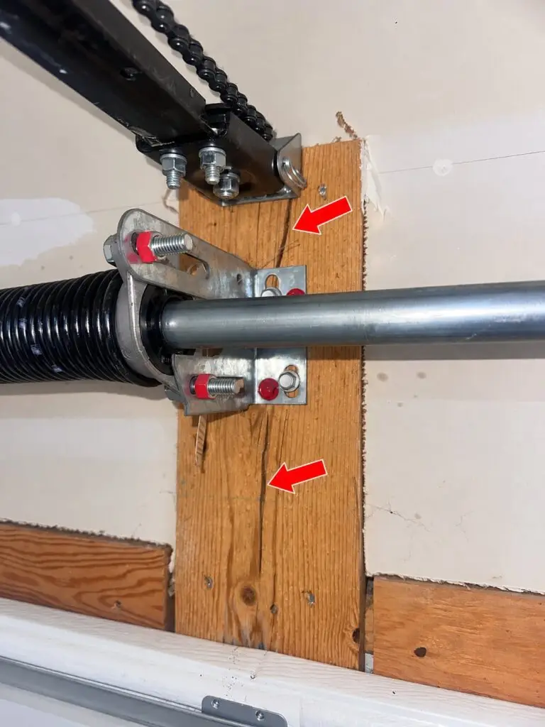 Split garage door spring pad behind a torsion spring center bracket and garage door opener header bracket.