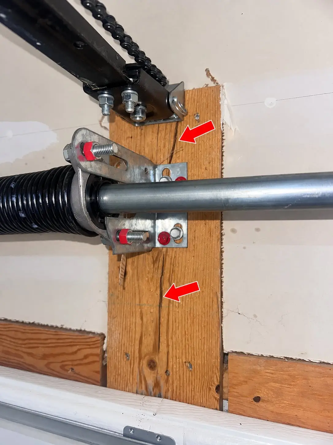 Split garage door spring pad behind a torsion spring center bracket and garage door opener header bracket.